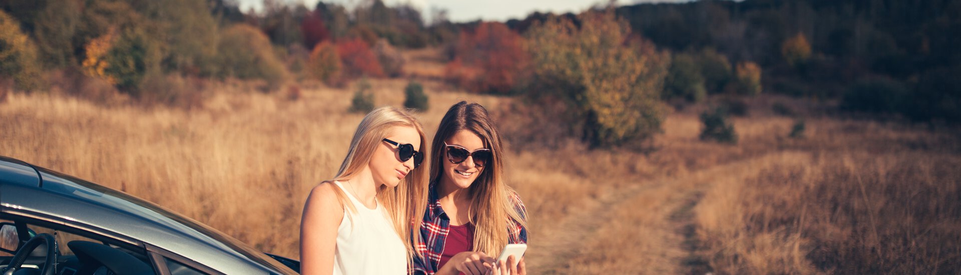 Teenager mit Handy vor Auto in herbstlicher Umgebung