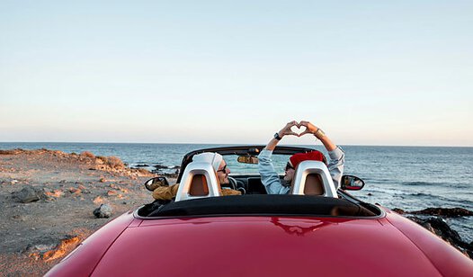 Junges Paar in rotem Cabrio von hinten auf hoher Steilküste