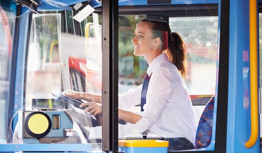 Gute gelaunte Busfahrerin mit weißem Hemd in blauem Bus 