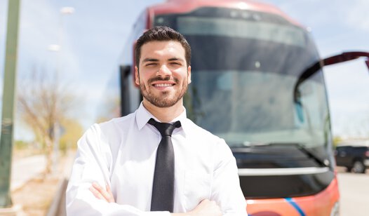 Bufahrer mit weißem Hemd steht vor unscharfem Reisebus im Hintergrund